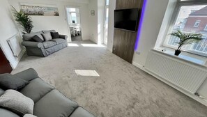 A living room with a grey sofa, a flat-screen TV mounted on the wall, and a window with blinds. - Large luxury property, sea view (East Riding of Yorkshire)