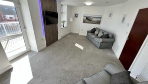 A living room with a grey sofa, a flat-screen TV mounted on the wall, and a window with blinds. - Large luxury property, sea view (East Riding of Yorkshire)