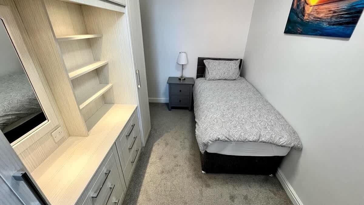 Ein Schlafzimmer mit Bett, Nachttisch, Lampe und integriertem Bücherregal.