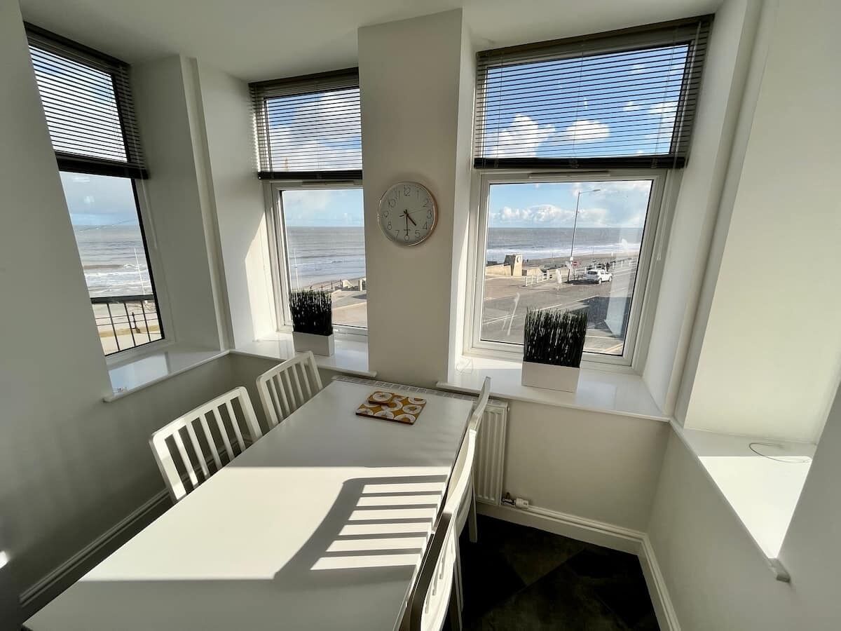 Una habitación con una mesa de comedor, sillas, un reloj y vistas al mar a través de amplios ventanales.