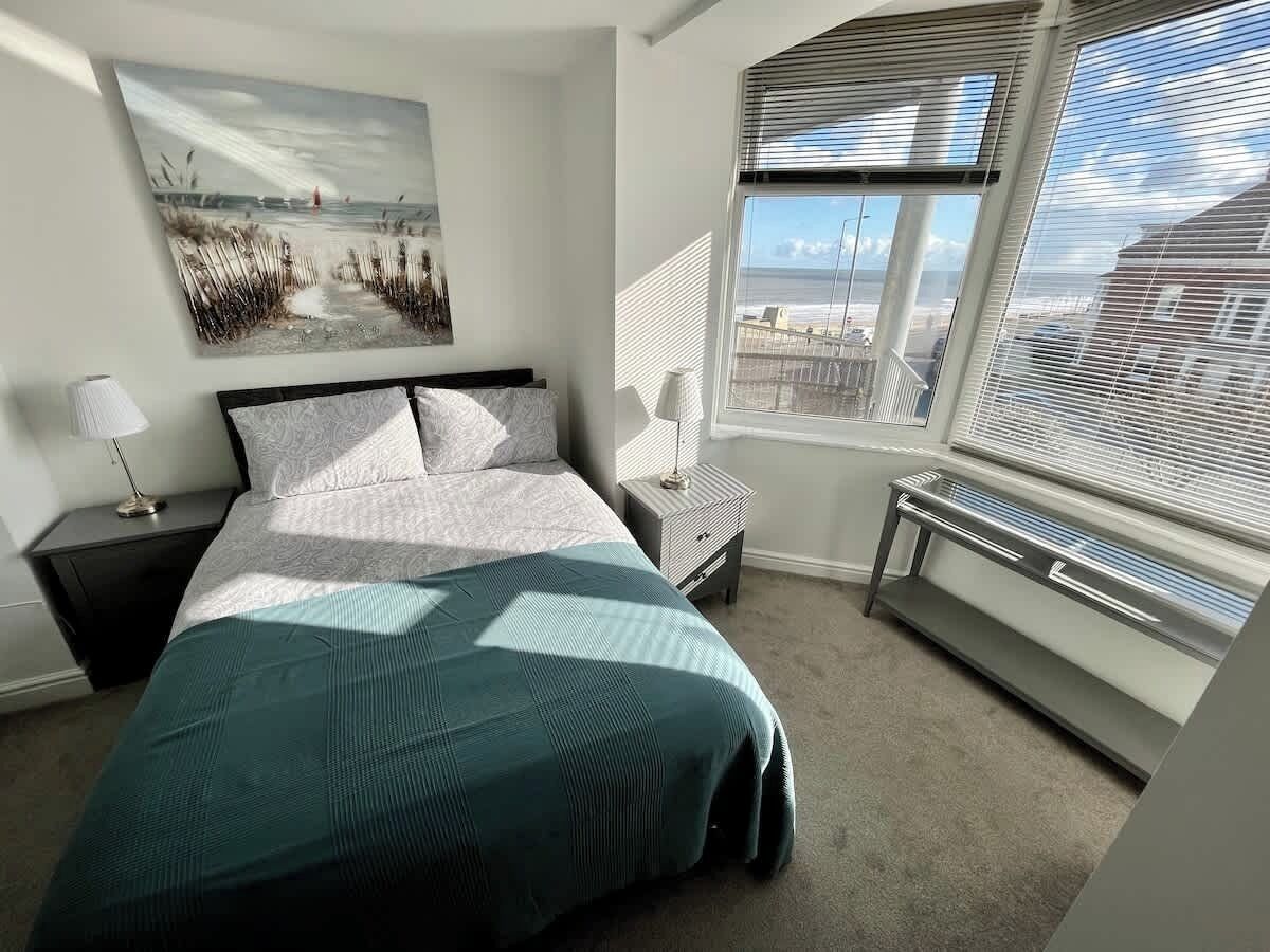 Une chambre à coucher comprenant un lit, une table de chevet, une chaise, une fenêtre avec des stores et un radiateur.