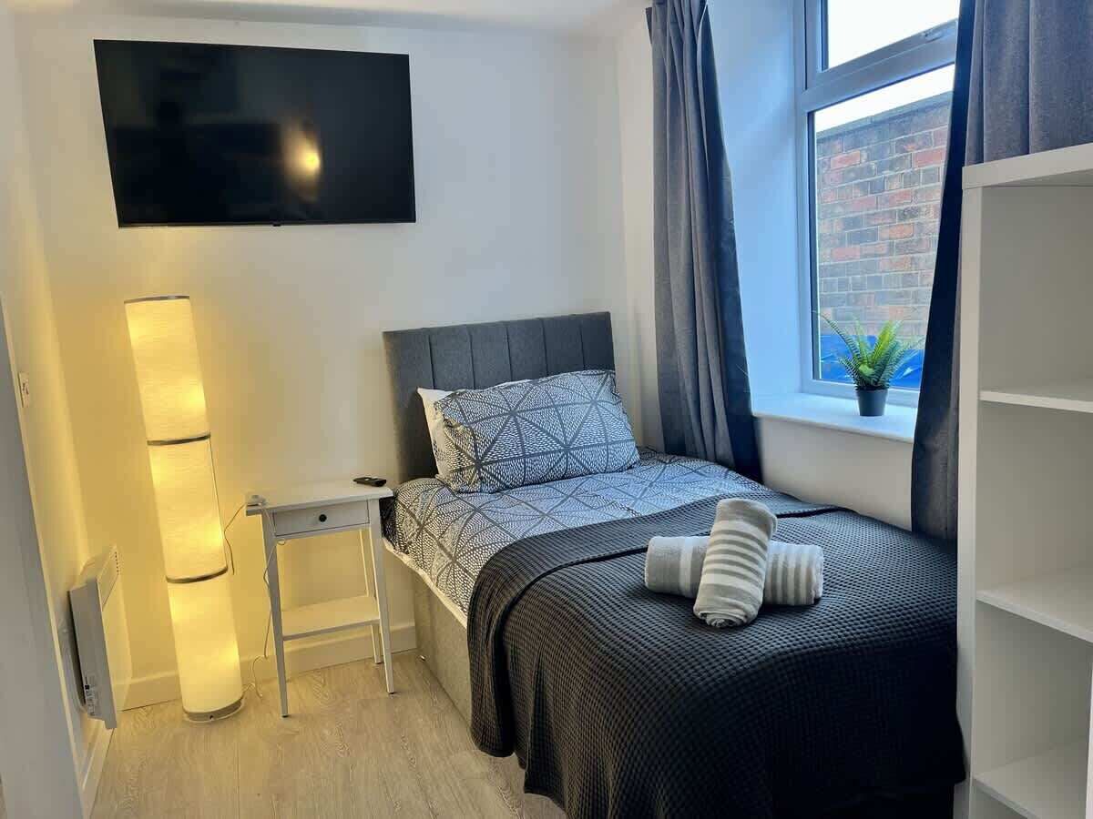 A modern bedroom with a bed, bedside table, lamp, and a TV mounted on the wall.