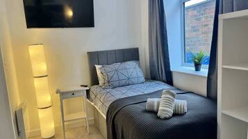 A modern bedroom with a bed, bedside table, lamp, and a TV mounted on the wall.