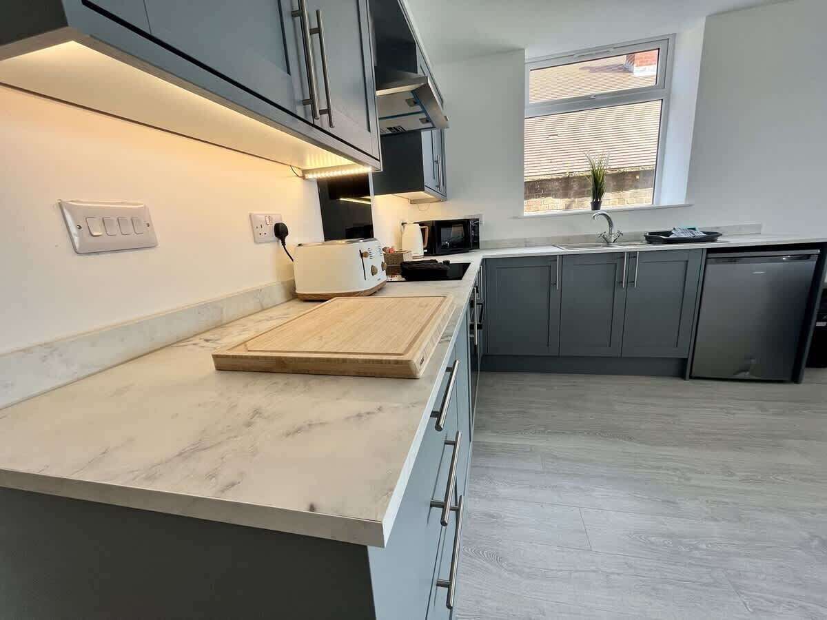 A modern kitchen with grey cabinets, a marble countertop, and a window providing natural light.