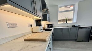 A modern kitchen with grey cabinets, a marble countertop, and a window providing natural light. - Seaside Escapes Apt. 2 (East Riding of Yorkshire)