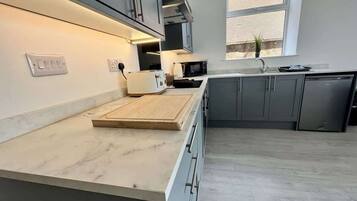 A modern kitchen with grey cabinets, a marble countertop, and a window providing natural light.