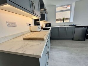A modern kitchen with grey cabinets, a marble countertop, and a window providing natural light. - Seaside Escapes Apt. 2 (East Riding of Yorkshire)