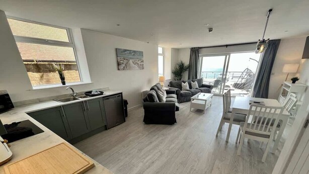 A modern living space with a kitchen, dining area, and seating area, featuring a large window and a view of the outdoors. - Seaside Escapes Apt. 2 (East Riding of Yorkshire)