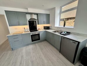 A compact kitchen with grey cabinets, a built-in oven, a microwave, and a dishwasher. - Seaside Escapes Apt. 2 (East Riding of Yorkshire)