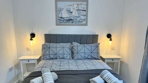 A neatly made bed with a geometric patterned bedspread, two bedside lamps, and a framed artwork above the bed. - Seaside Escapes Apt. 2 (East Riding of Yorkshire)