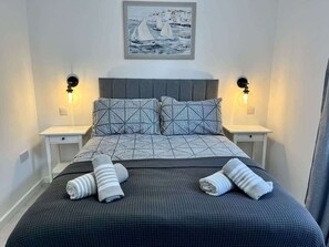 A neatly made bed with a geometric patterned bedspread, two bedside lamps, and a framed artwork above the bed. - Seaside Escapes Apt. 2 (East Riding of Yorkshire)