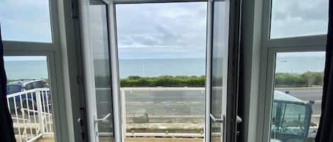 An open window with a view of a beach and a parking area.
