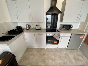 Eine kompakte Küche mit weißen Schränken, einer schwarzen Dunstabzugshaube, einer Mikrowelle, einem Toaster und einem Geschirrspüler.