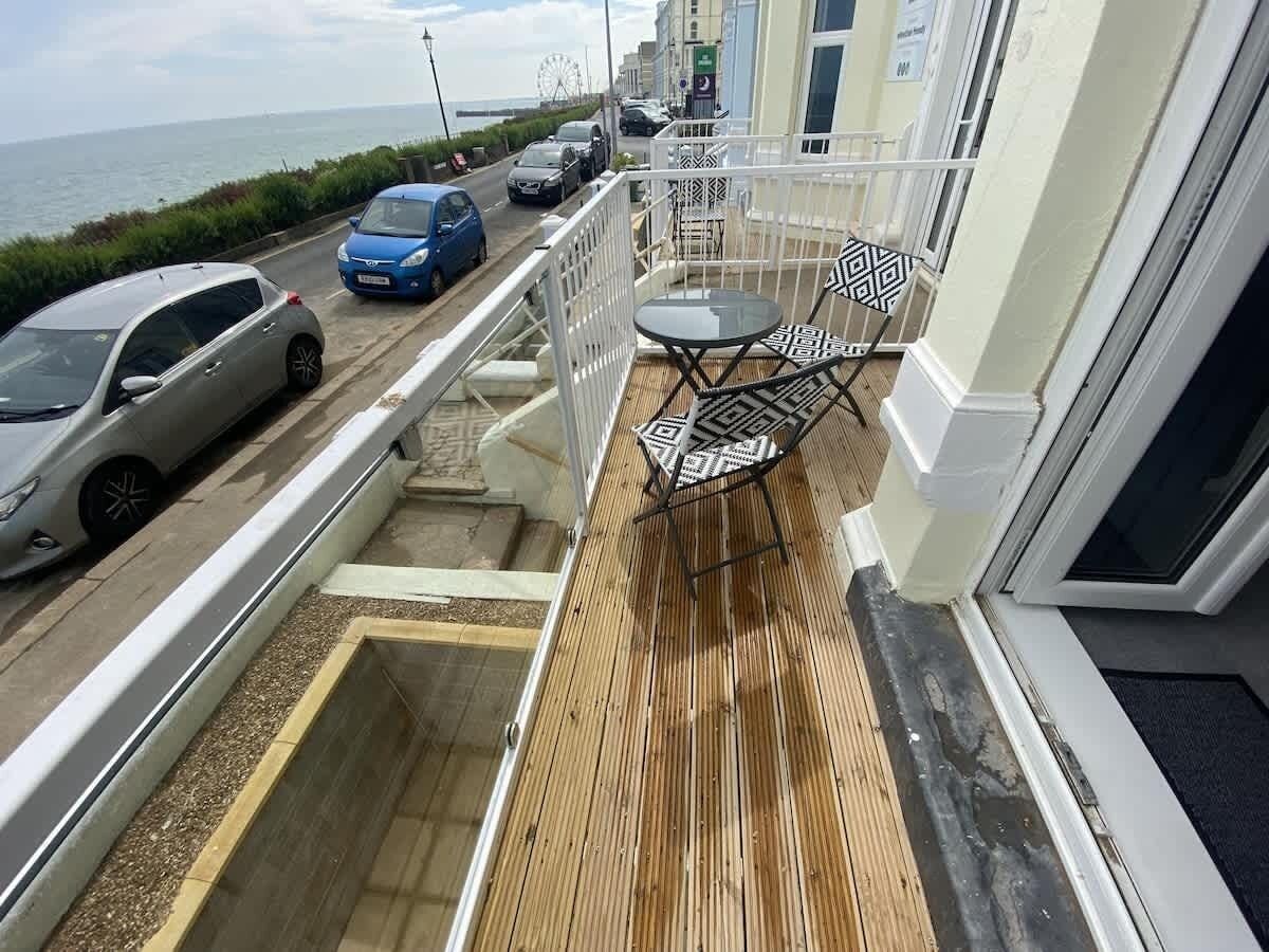 A balcony with a wooden deck, a table, and two chairs.