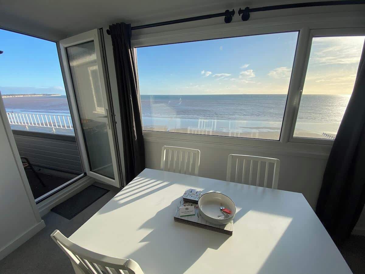 A room with a table, a bowl, and a book, overlooking a body of water.