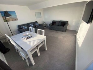 Ein kompakter Wohnraum mit Esstisch, zwei Sofas, einem Heizkörper und einem an der Wand befestigten Fernseher.