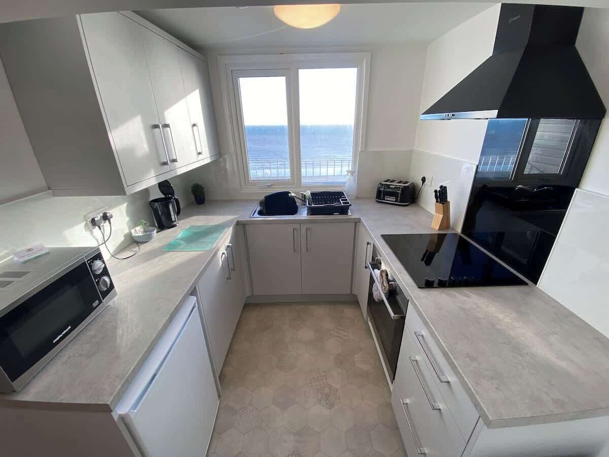 A compact kitchen with a view of the sea, a microwave, a toaster, and a black range hood.