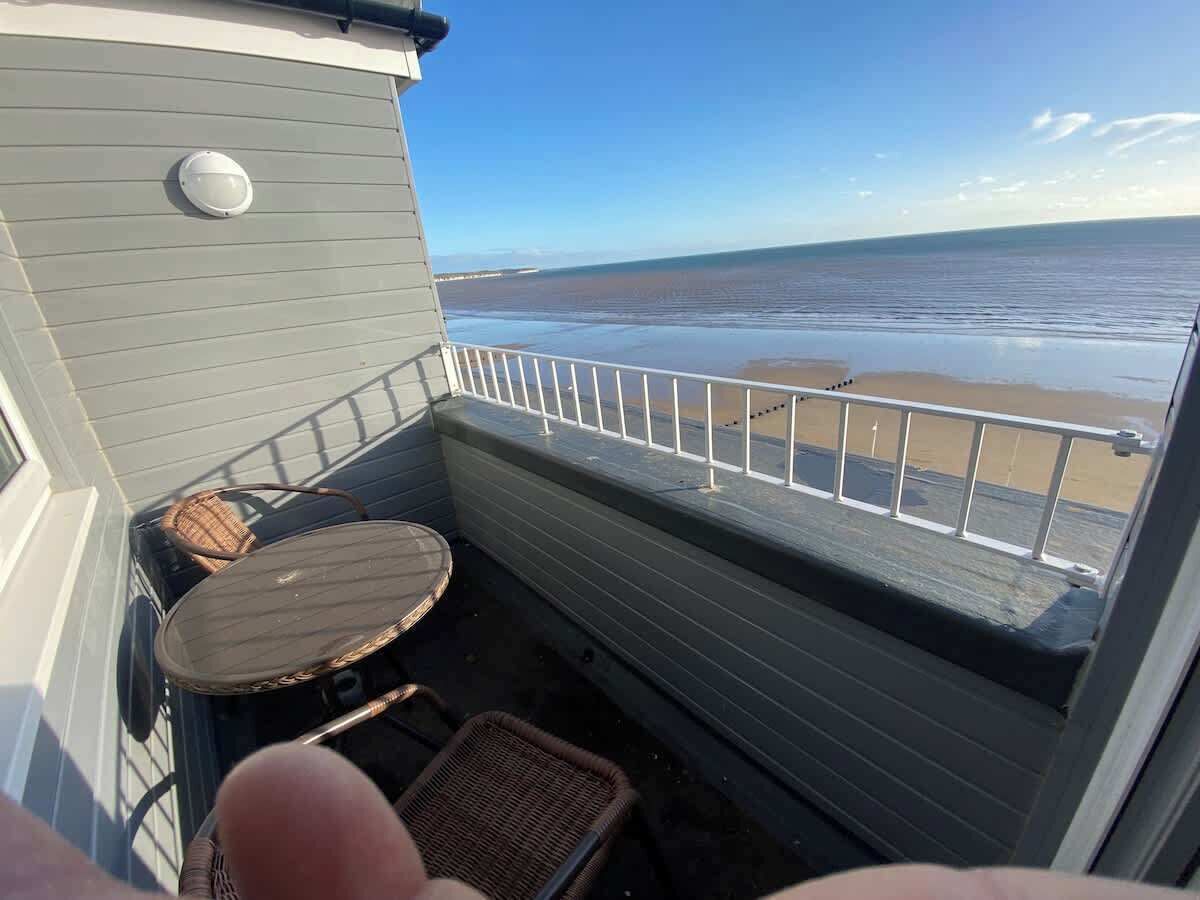 Un balcon avec vue sur la plage, une table ronde et deux chaises en osier.