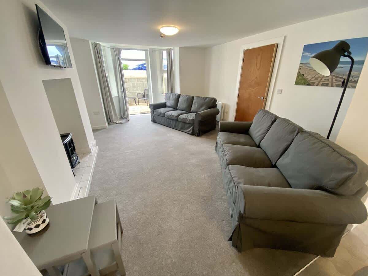 A living room with a grey sofa, a television mounted on the wall, and a door leading to an outdoor area.