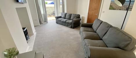 A living room with a grey sofa, a television mounted on the wall, and a door leading to an outdoor area.