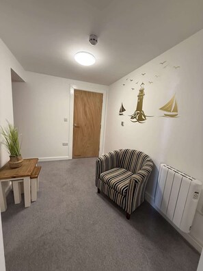 Ein Zimmer mit einem gestreiften Sofa, einem Holztisch mit einer Pflanze, einem weißen Heizkörper und einer Tür zu einem anderen Raum.