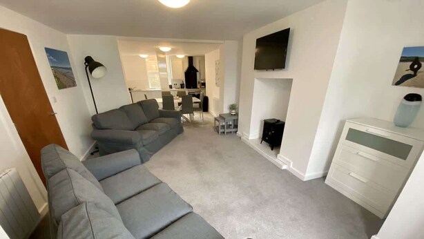 Ein Wohnzimmer mit einem grauen Ecksofa, einem Kamin und einem an der Wand montierten Fernseher.