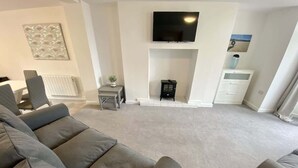 Ein Wohnzimmer mit einem großen grauen Sofa, einem Flachbildfernseher über einem Kamin und einem weißen Heizkörper.