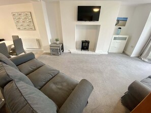 Ein Wohnzimmer mit einem großen grauen Sofa, einem Flachbildfernseher über einem Kamin und einem weißen Heizkörper.