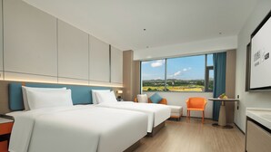 Habitación de hotel con dos camas, un escritorio, una silla y un amplio ventanal con vistas a la ciudad.