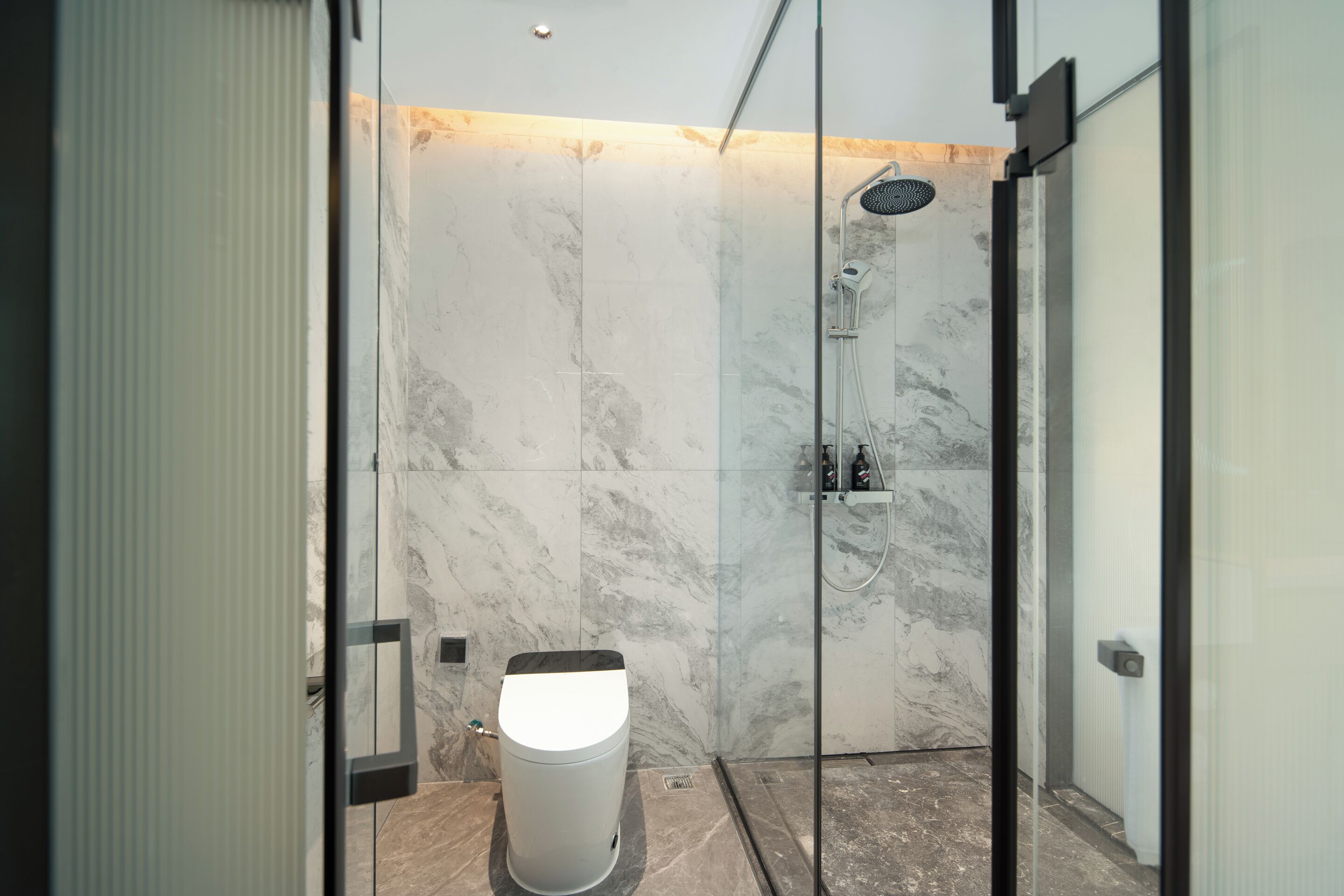 Une salle de bain moderne avec une douche à parois de verre, des murs en marbre et des toilettes.