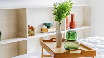 A bedroom with a bed, a wooden bedside table with a vase and a green glass, and a wall with decorative wooden items.