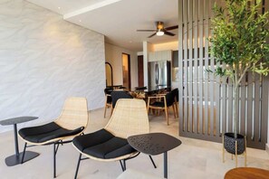 A modern interior with two lounge chairs, a dining area, and a decorative plant. - Apt Huico: Ocean Views, Shared Rooftop & Pool (Puerto Morelos)