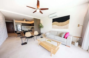 A modern living room with a sofa, coffee table, and chairs, a dining area with a table and chairs, and a kitchen in the background. - Apt Huico: Ocean Views, Shared Rooftop & Pool (Puerto Morelos)