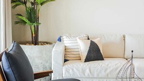 En moderne stue med en sofa, en træstol, et lille bord og en potteplante.