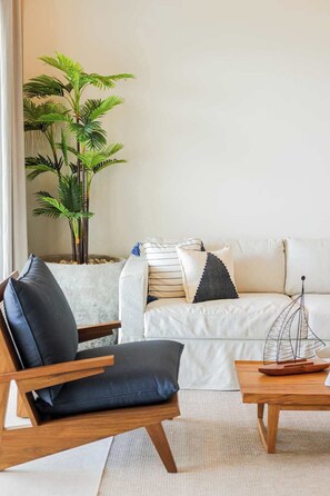 Ein modernes Wohnzimmer mit einer Couch, einem Holzstuhl, einem kleinen Tisch und einer Topfpflanze.