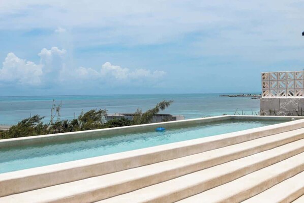 Ein klarer, blauer Himmel, ein Pool mit Stufen und Blick auf den Ozean.