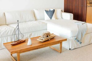 Ein modernes Wohnzimmer mit einem weißen Sofa, einem Holztisch mit Dekoration und einem Bett mit weißer Bettdecke.