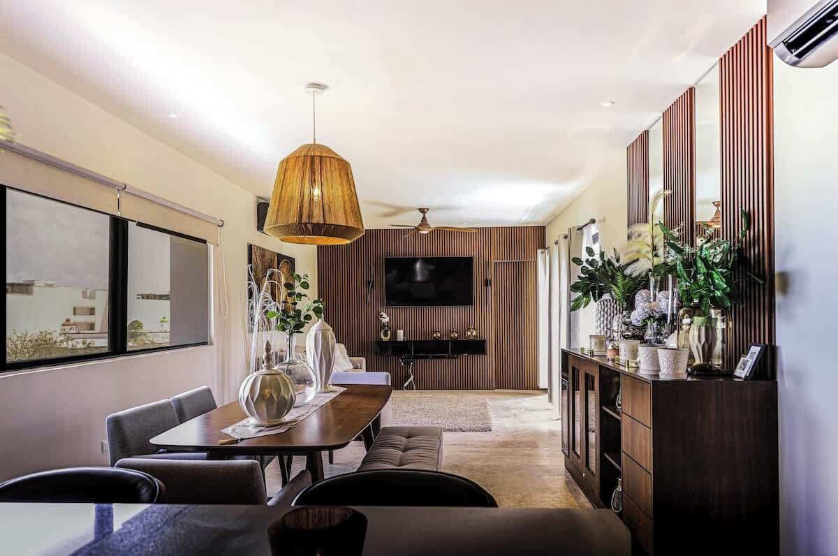 A modern living room with a dining area, a TV mounted on a wooden wall, and a ceiling fan.