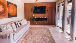 Un soggiorno moderno con un divano, televisione, ventilatore a soffitto e un'ampia finestra con tende.