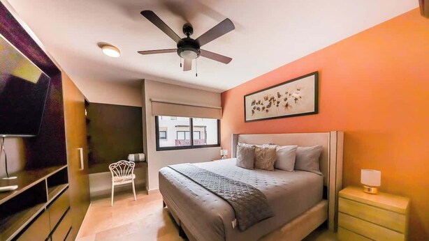 Una camera da letto con un letto, una ventola a soffitto, un comodino, una sedia e una finestra.