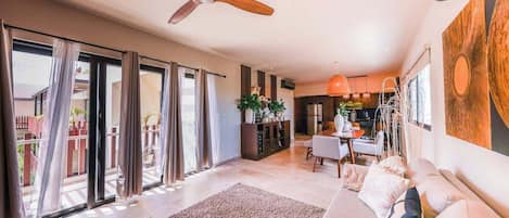 A spacious living area with a sofa, a dining table, and a ceiling fan.