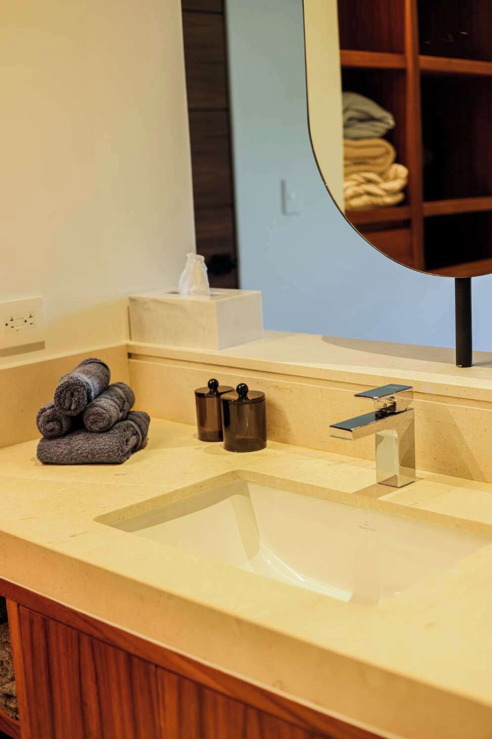 Un baño con encimera color beige, un lavamanos, un espejo y una pila de toallas.