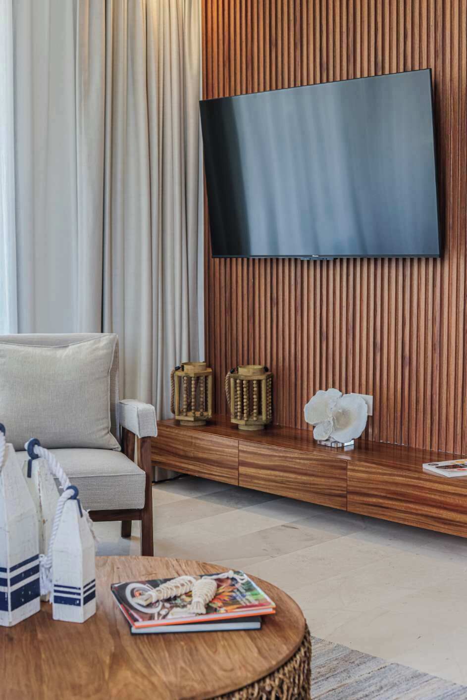 A modern living room with a flat-screen TV mounted on a wooden wall, a comfortable sofa, and a round coffee table with a magazine.