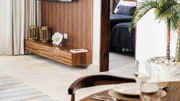 Een moderne woonkamer met een flatscreen televisie aan een houten wand, een eethoek met een tafel gedekt voor twee personen, en een slaapkamer zichtbaar door een open deur.