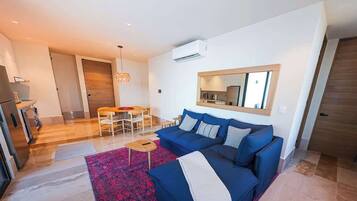 A modern living room with a blue sofa, a dining area with a wooden table, and a kitchen in the background.