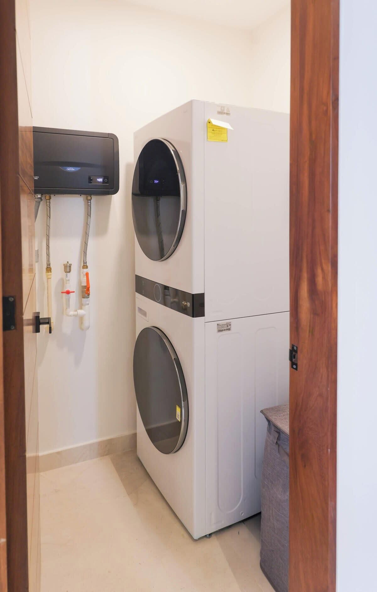 A laundry room with two stacked washing machines, a water heater, and a trash bin.