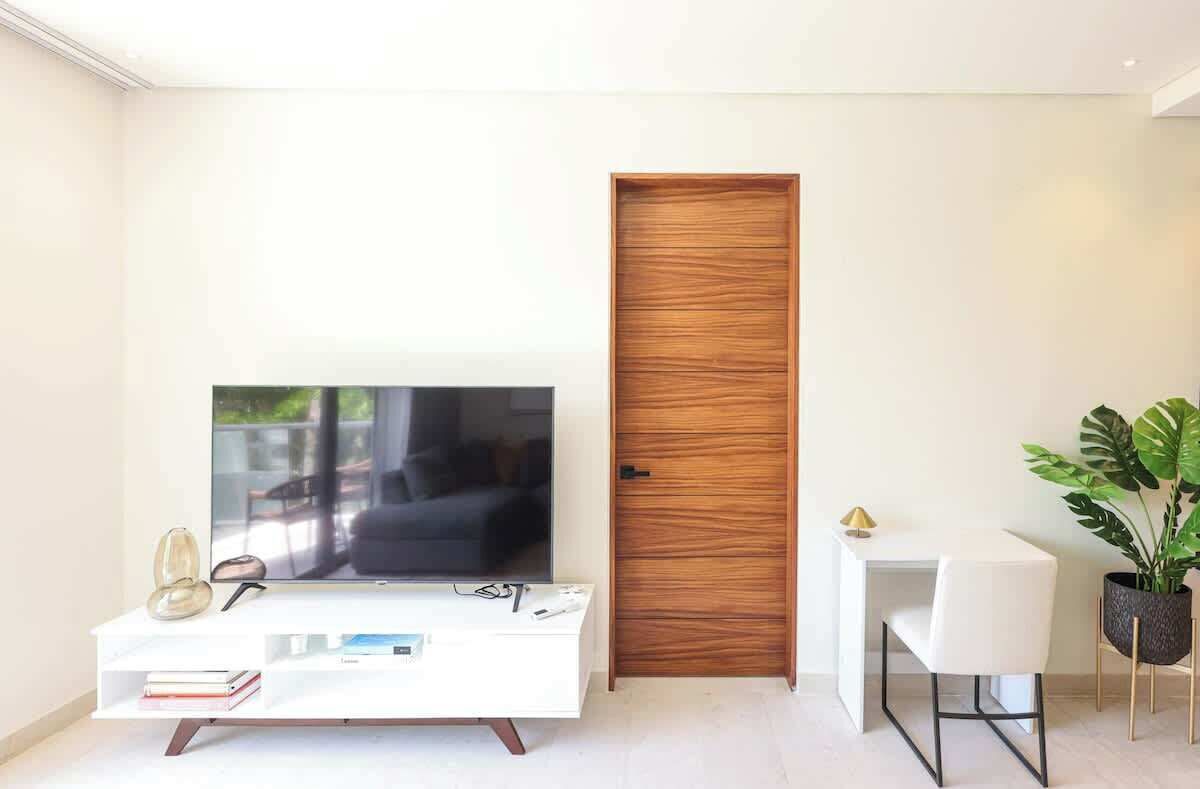 Un salon moderne avec un téléviseur à écran plat, une console blanche, une porte en bois et une plante en pot.