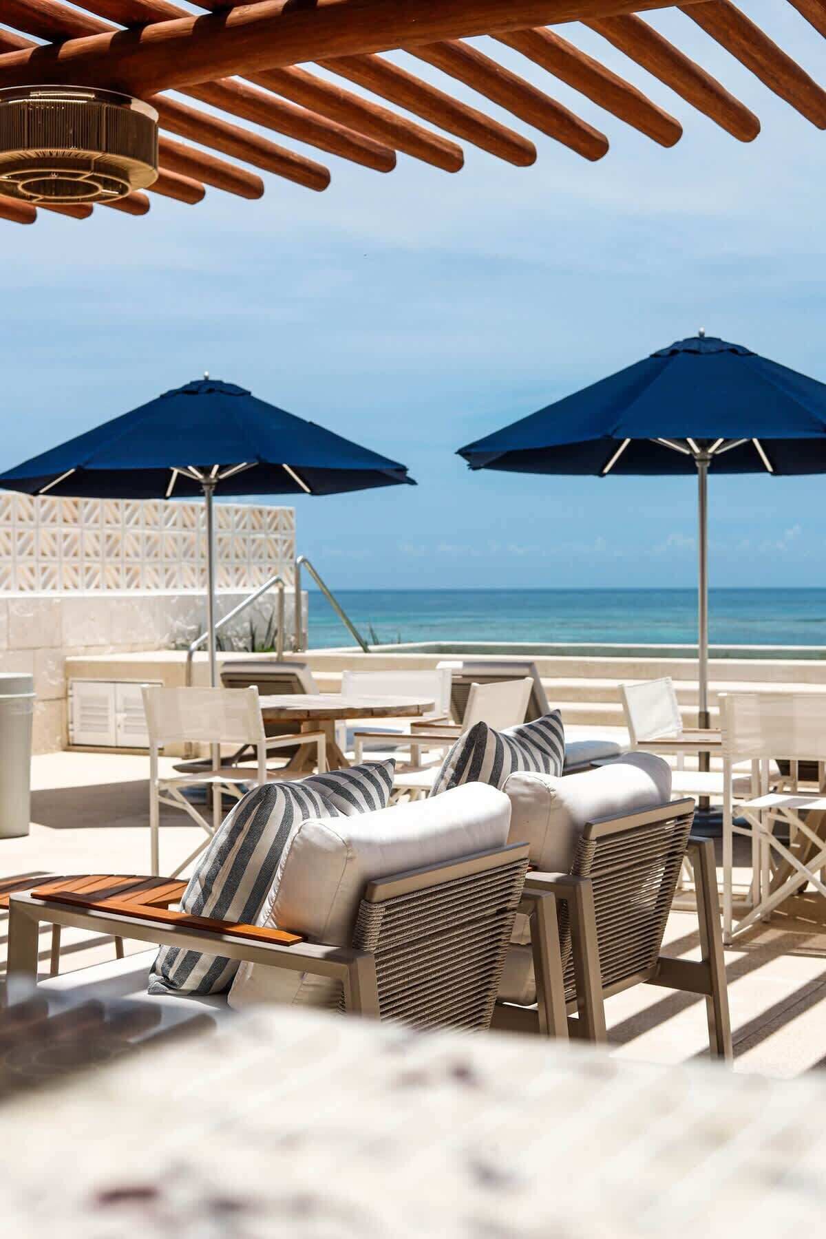 Un salon de plage équipé de deux parasols, de chaises longues et offrant une vue sur l’océan.