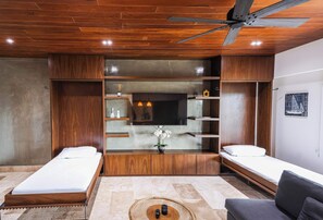A modern room with two beds, a TV, wooden shelving, and a ceiling fan.