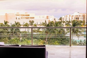 A hotel room with a balcony, a view of palm trees, and a building in the background. - La Amada | Rooftop Condo w Marina & Mangrove Views (Cancún)